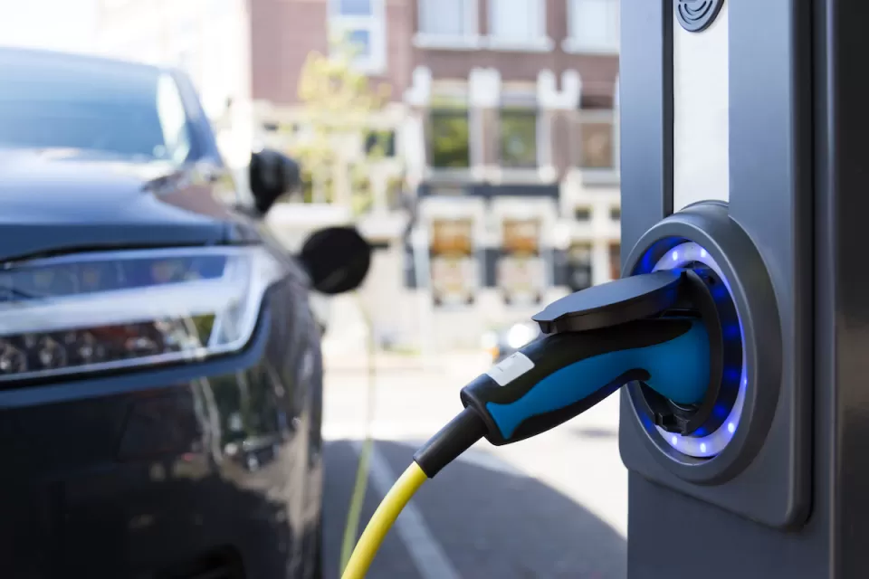 Close-up of electric car charging port with blurred dark colored car in background.